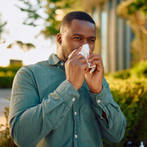 portrait of a man sneezing while outside and suffering from spring allergies