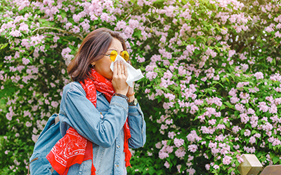 Young asian woman sneezes and blowing her nose with a handkerchief and suffering in the spring among flowering and blooming trees.