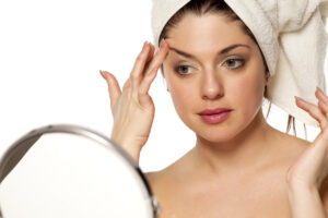 woman looking in the mirror at her thinning eyebrows