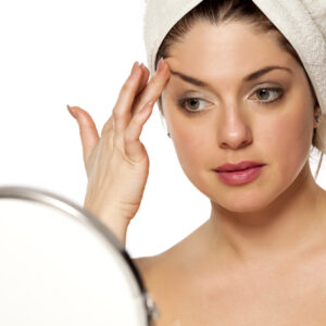 woman looking in the mirror at her thinning eyebrows