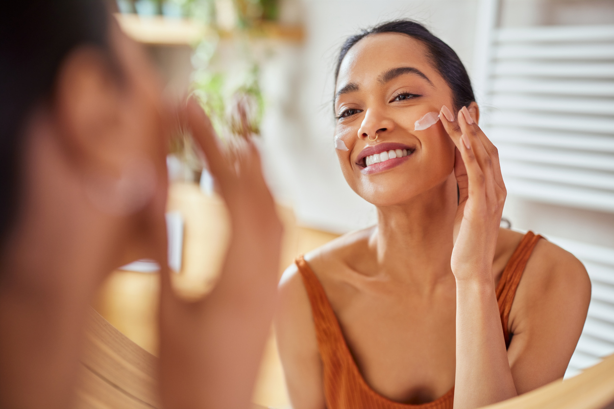 woman looking in the mirror while applying medical-grade skin care as recommended by a dermatologist