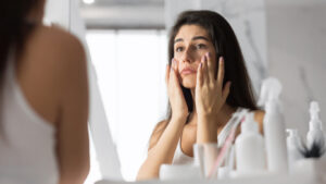 Woman looking in her bathroom mirror while touching her face and wondering why her skin is so sensitive