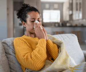 Cold sick woman sitting indoor suffering from allergy and blowing nose