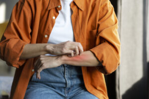 closeup shot of a woman in an orange shit itching her forearm that has eczema