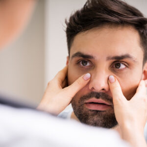 Close up of an allergist with his hands on a patient's face to decipher and diagnose allergies vs sinus infection