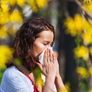 Photo of a woman sneezing into a tissue while outside during March allergy season