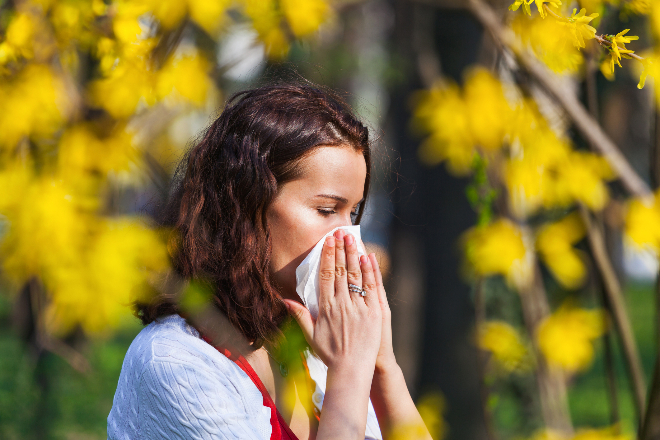 Photo of a woman sneezing into a tissue while outside during March allergy season