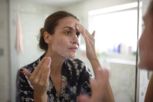 Young female in the bathroom looking in the mirror and taking care of her facial skin.